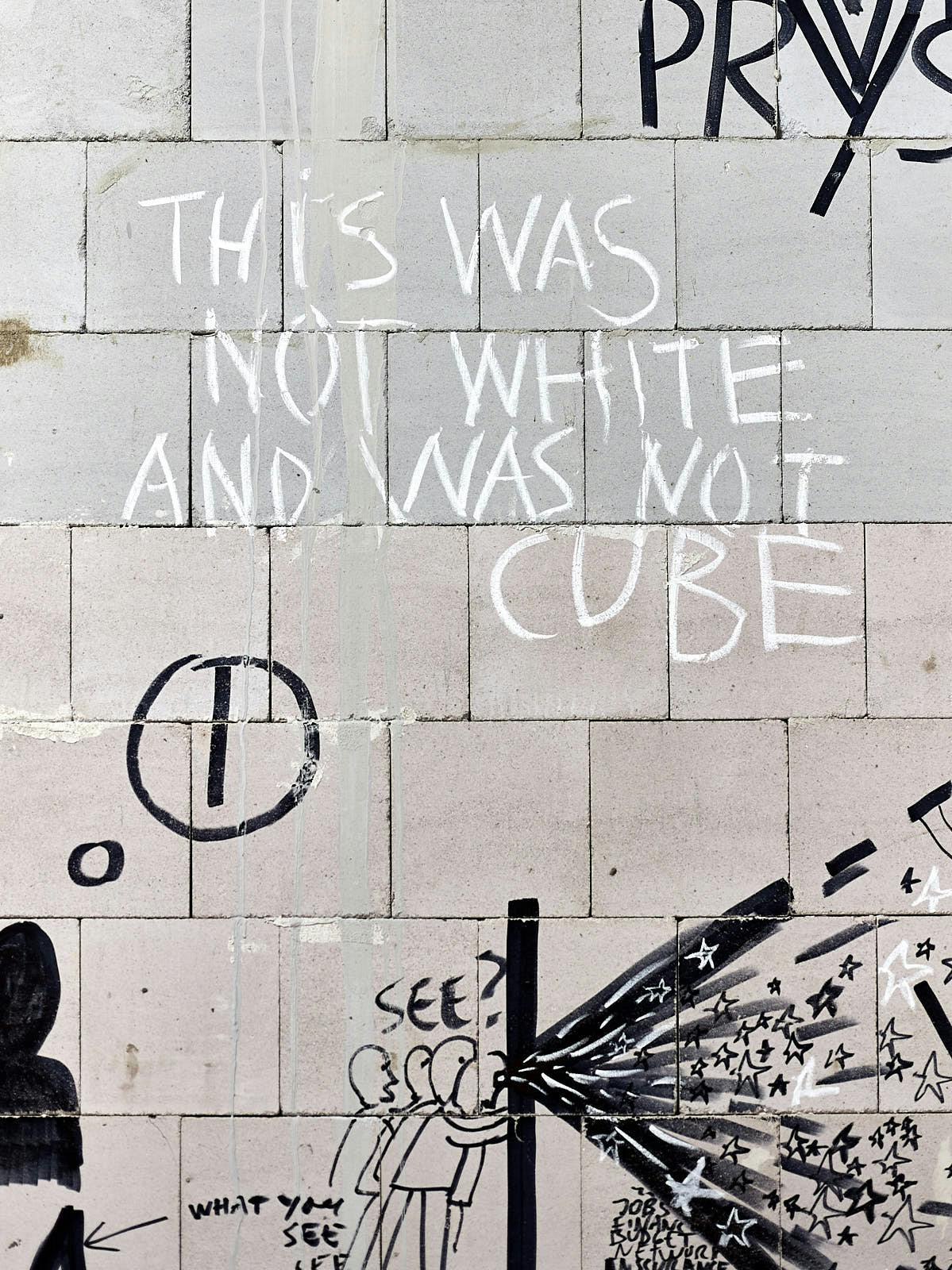 Foto: auf rohen, großen Betonwerksteinen sind schwarze Zeichnungen und die Worte This was not white and was not cube geschrieben.