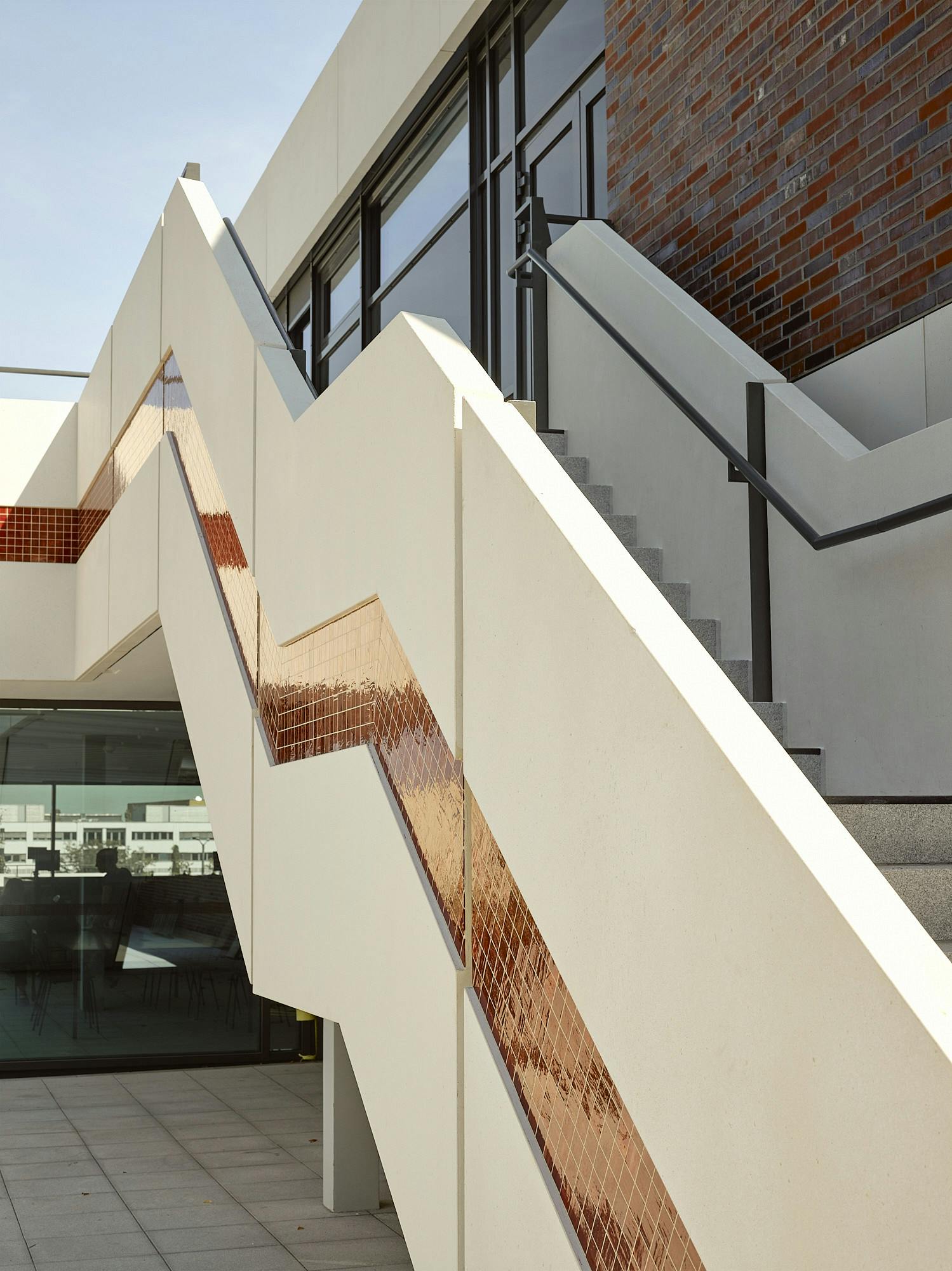 Photo: An external staircase leads to the second floor of DAS MINSK. The sides are covered with narrow white panels in which red mosaic pieces are embedded.