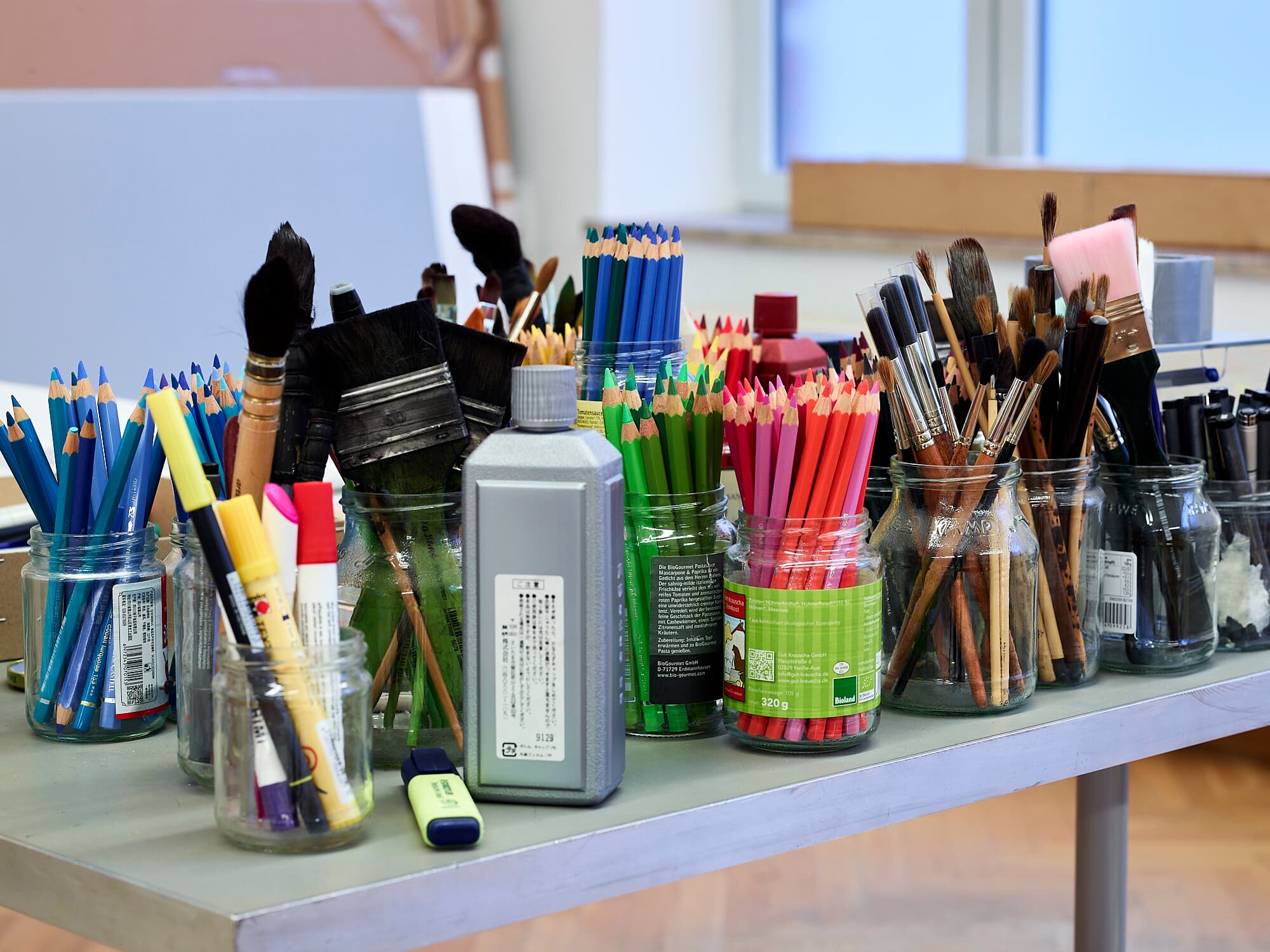 Foto, ein Innenraum: Alles ist für einen Kunst-Workshop vorbereitet. Gläser mit Pinseln, sowie Farben und weitere Malutensilien stehen bereit.