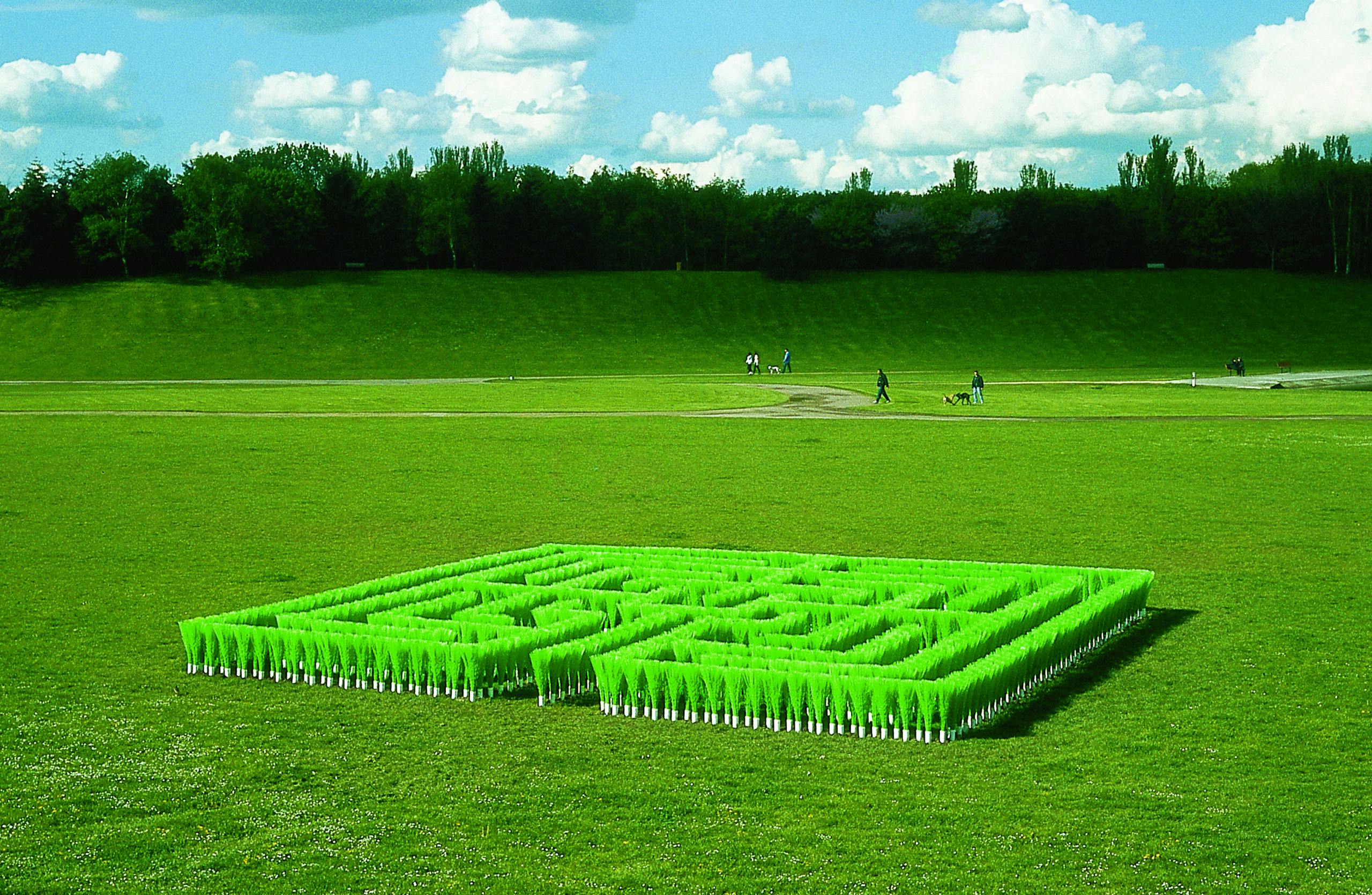 Installation of a square labyrinth made of green broom handles on a green area.